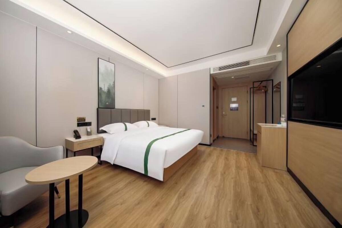 A modern hotel room with a bed, bedside table, chair, and a television.