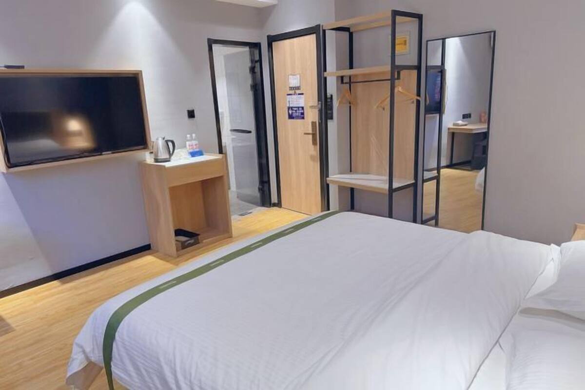 A hotel room with a bed, a TV, a wooden desk, a mirror, and a wardrobe.