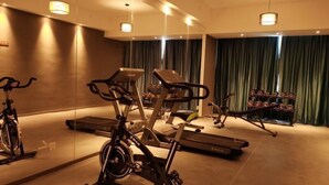 A gym with exercise equipment, including treadmills and an elliptical, in a room with mirrors and green curtains. - Greentree Eastern Changge Yiwu City Hotel (Xuchang)