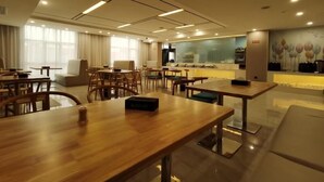 A modern hotel lobby with wooden tables and chairs, a seating area with a sofa, and a counter with a mural. - Greentree Eastern Changge Yiwu City Hotel (Xuchang)