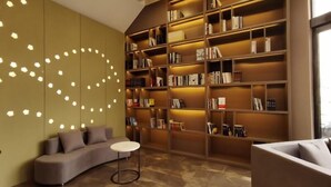 A modern interior with a curved sofa, a small round table, and a large bookshelf filled with books. - Greentree Eastern Changge Yiwu City Hotel (Xuchang)