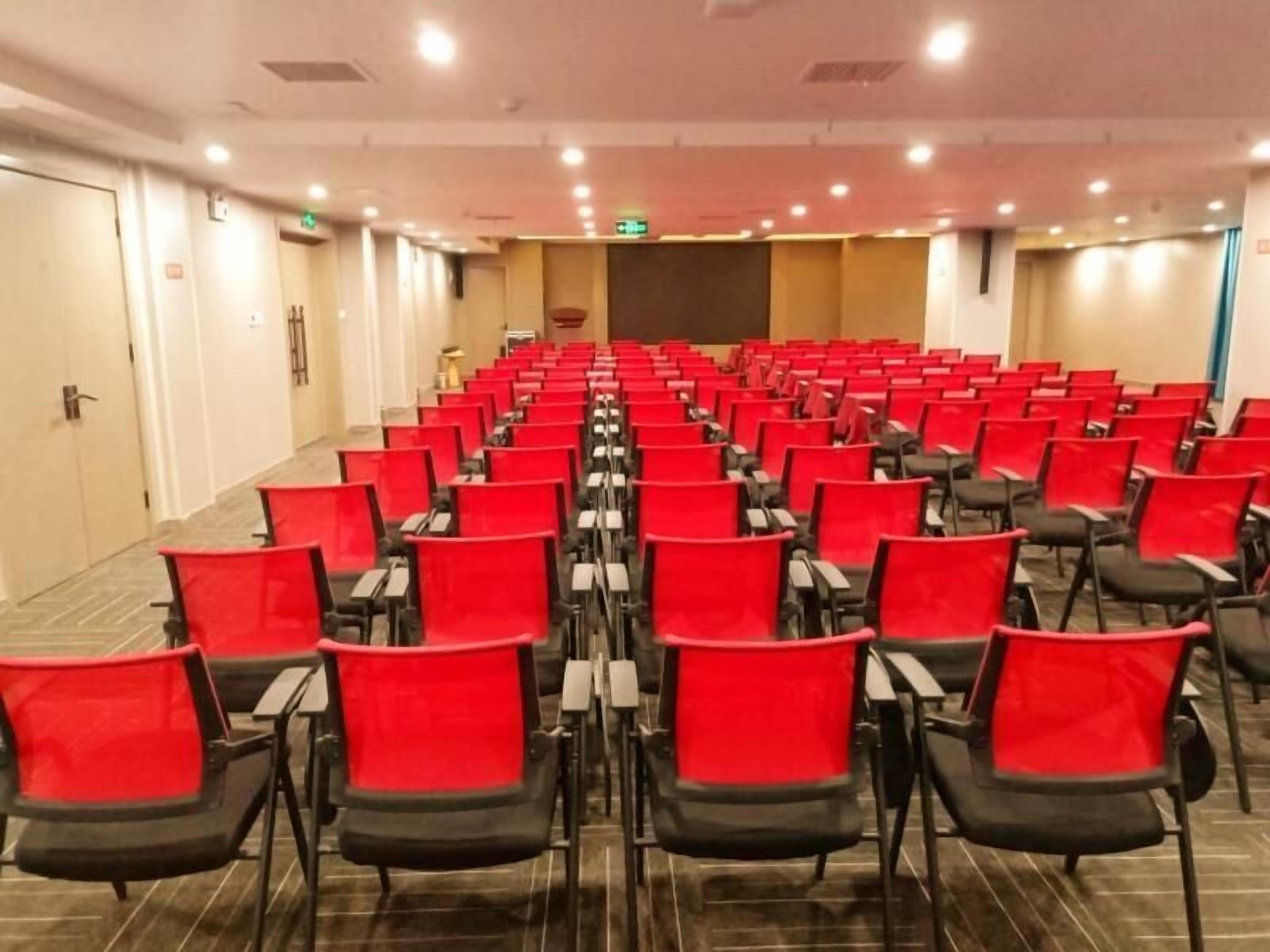 A conference room with rows of red chairs and a stage at the front.
