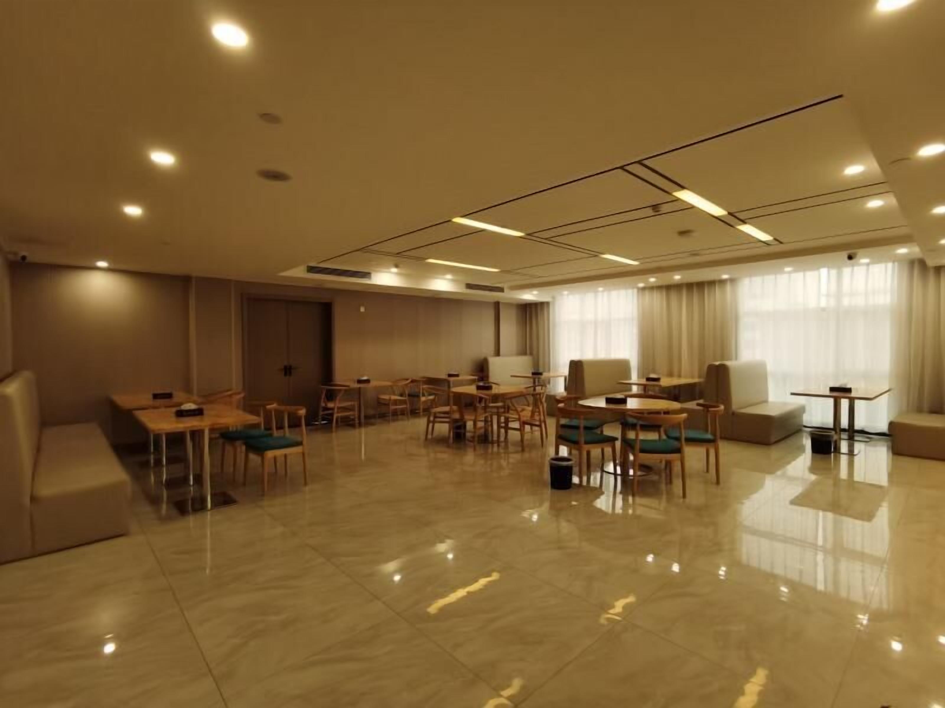 Habitación de hotel moderna con una amplia zona de estar bien iluminada, múltiples opciones de asiento y un gran ventanal con cortinas.
