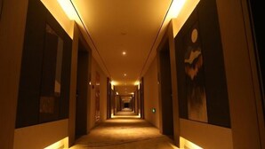A hotel hallway with a carpeted floor, illuminated by overhead lighting, and flanked by walls with framed artwork. - Greentree Eastern Changge Yiwu City Hotel (Xuchang)