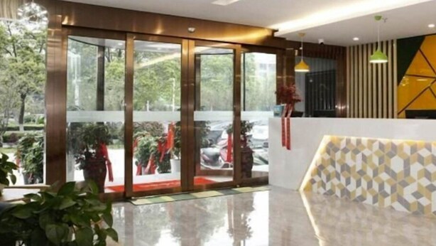 A modern hotel lobby with a glass entrance, a reception desk, and a view of the outdoors. - Vatica Hotel Anqing Wuyue Square Boai Hospital (Anqing)
