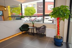 A hotel lobby with a large window, two chairs, a small table, and a potted plant.