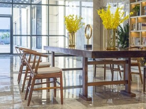 A modern interior with a glass table and wooden chairs, a bookshelf, and yellow flowers in vases. - Greentree Eastern Hotel Hainan Free Trade Port Jiangdong New District Meilan Airport (Luzhou)