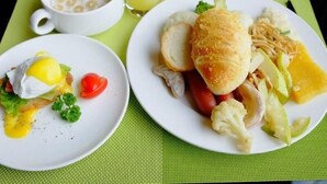 Una mesa con huevos, salchichas y verduras, un tazón de cereal y un vaso de jugo.
