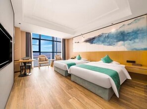 Habitación de hotel con dos camas, televisión, escritorio y ventana grande con vistas.