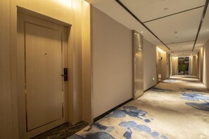 Pasillo de hotel con alfombra estampada, puertas de madera y un diseño moderno en el techo.