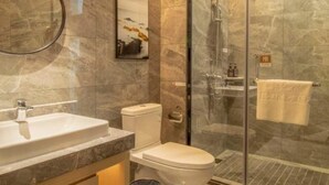 Un baño moderno con cabina de ducha de vidrio, lavamanos blanco y retrete.