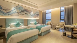 Habitación de hotel con dos camas, un cuadro abstracto grande, vistas de la ciudad y una zona de comedor.