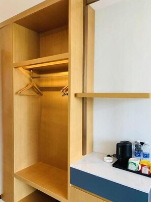 Une armoire en bois avec un espace pour suspendre des vêtements et un plan de travail sur lequel se trouvent une bouilloire, une tasse et une bouteille.