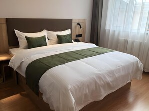 A neatly made bed with white and green bedding, a wooden headboard, and a bedside table with a lamp. - Greentree Inn Qingdao Laixi High-speed Railway Station Shenzhen Road Express Hotel (Qingdao)