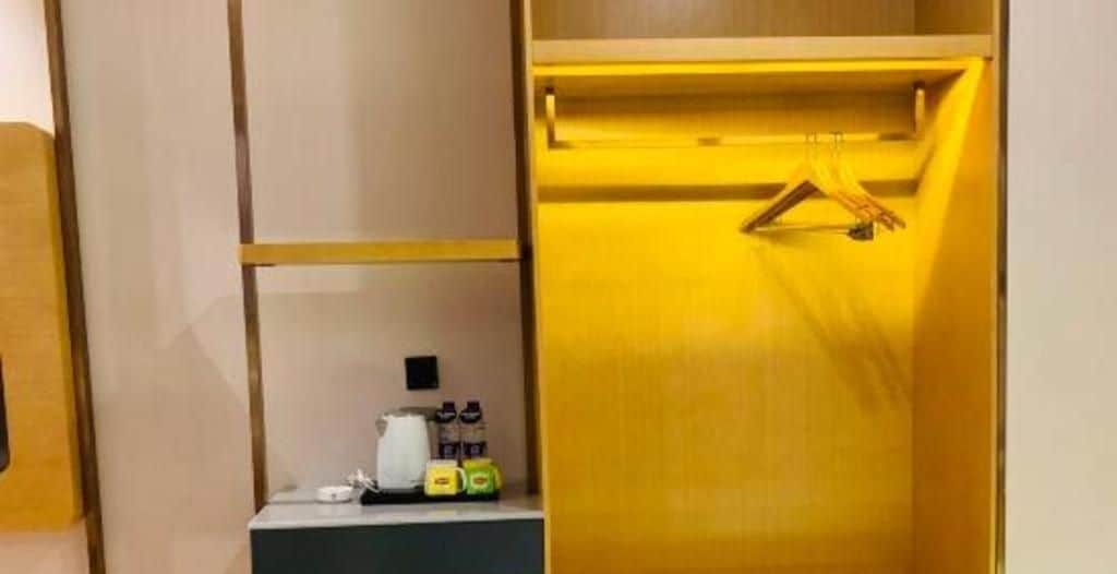 A wooden wardrobe with a hanging rod, a shelf with a basket, and a small countertop with a kettle and bottles.