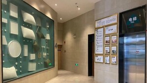A modern lobby with a glass display of various items, a wall-mounted information board, and a stainless steel elevator. - Greentree Inn Fuyang Yinzhou District Nanjing Road Teachers College (Fuyang)