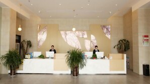 A reception area with two receptionists, a white reception desk, and potted plants. - Greentree Inn Fuyang Yinzhou District Nanjing Road Teachers College (Fuyang)