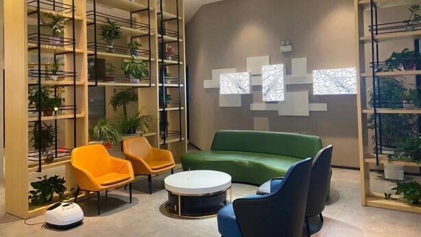 A modern interior with a green sofa, two orange chairs, a round coffee table, and a wall with abstract art. - Greentree Inn Fuyang Yinzhou District Nanjing Road Teachers College (Fuyang)