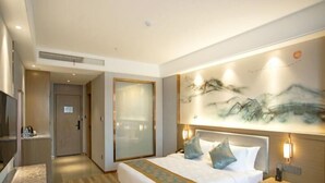 A hotel room with a bed, bedside table, and a large painting on the wall.