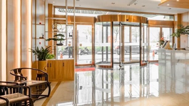 A hotel lobby with a glass elevator, wooden paneling, and a seating area with chairs.