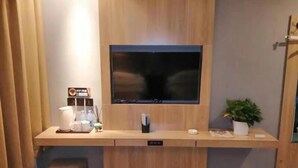 A hotel room with a wooden desk, a television, a small stool, a potted plant, and a trash bin. - Shell Cangzhou Nanpi County Hospital of Traditional Chinese Medicine Hotel (Cangzhou)