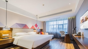 Habitación de hotel moderna con una cama grande, un escritorio, una silla y vistas a la ciudad por la ventana.