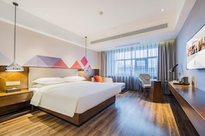 Una camera d'hotel moderna con un letto grande, una scrivania, una sedia e vista sulla città dalla finestra.