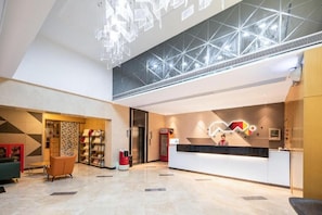 A hotel lobby with a reception desk, seating area, and a patterned wall.