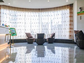 Eine Hotelhalle mit einer Rezeption, einer Sitzecke mit Sesseln und einem großen Fenster mit Vorhängen.