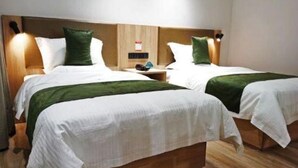 A hotel room with two beds, each with a wooden headboard, white bedding, and green throw pillows. There is a nightstand with a lamp and a small table between the beds. - Greentree Inn Xi an Baqiao District Hongqing Business Hotel (Xi'an)