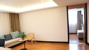 A modern living room with a wooden floor, a sofa with cushions, a small table with a plant, and a chair. - Greentree Inn Xi an Baqiao District Hongqing Business Hotel (Xi'an)