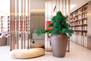 A modern interior with a large potted plant, wooden furniture, and a bookshelf. - Ji Hotel (Nanjing)