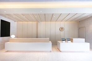 Una moderna zona de recepción con diseño minimalista, que incluye mostrador de recepción, área de estar y un logotipo montado en la pared.