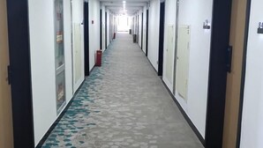 Un largo y estrecho pasillo de hotel con puertas a ambos lados, un suelo estampado e iluminación empotrada en el techo.