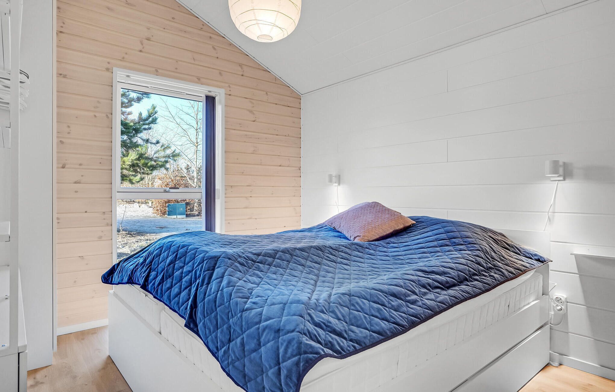 Un dormitorio con una cama, una ventana y una pared blanca.