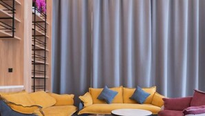 Een moderne woonkamer met een gele zithoek, een rode fauteuil en een kleine ronde tafel.