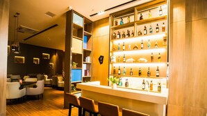 A bar area with a wooden floor, bar stools, and a shelf with various bottles.