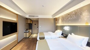 Ein modernes Hotelzimmer mit zwei Betten, einem an der Wand montierten Fernseher, einem Badezimmer mit Spiegel und einer dekorativen Wandverkleidung.