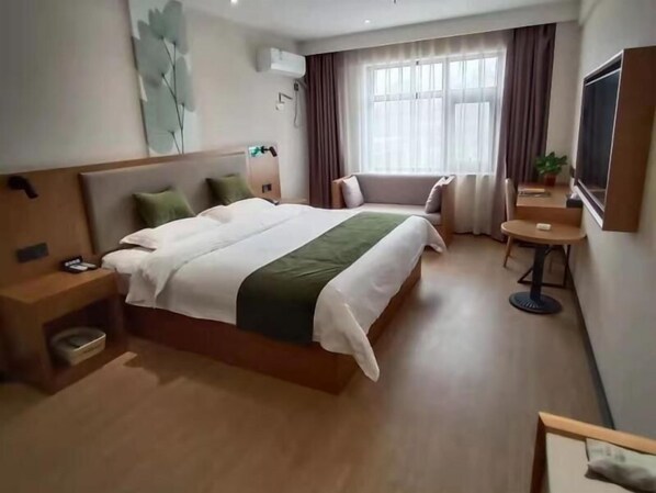 A hotel room with a large bed, a bedside table, a small round table, and a TV mounted on the wall. - Green Haotai Zhixuan Hotel (Shangqiu)