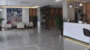 A modern reception area with a white reception desk, seating area with sofas, a large abstract mural, and a plant.