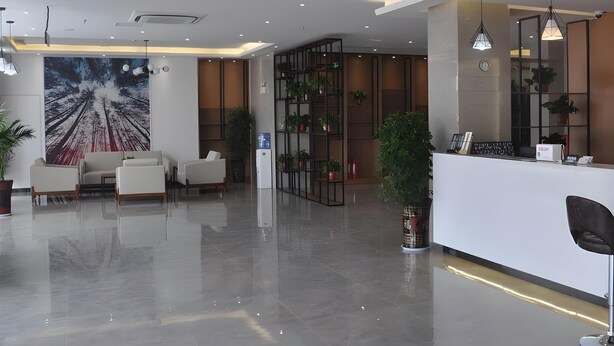 Un área de recepción moderna con un mostrador blanco, zona de estar con sofás, un gran mural abstracto y una planta.