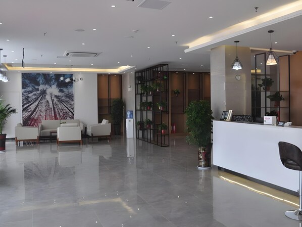 A modern reception area with a white reception desk, seating area with sofas, a large abstract mural, and a plant.