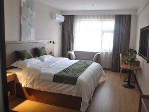 A hotel room with a large bed, a bedside table, a chair, a small table with a plant, and a window with curtains. - Green Haotai Zhixuan Hotel (Shangqiu)
