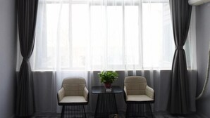 Une pièce moderne avec deux fauteuils et une petite table, de grandes fenêtres avec des rideaux légers et un climatiseur fixé au mur.