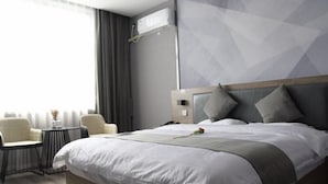 Een moderne hotelkamer met een groot bed, een nachtkastje, een stoel en een raam met gordijnen.
