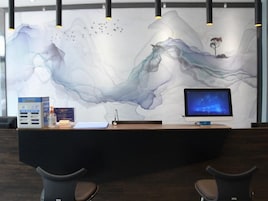 Un mostrador de recepción con un monitor de computadora, una caja de folletos y una pared con arte abstracto.