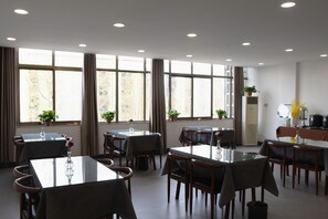A dining area with multiple tables and chairs, large windows with curtains, and potted plants. - Shell Puyang City Nanle County Coach Station Guangming South Road Hotel (Puyang)