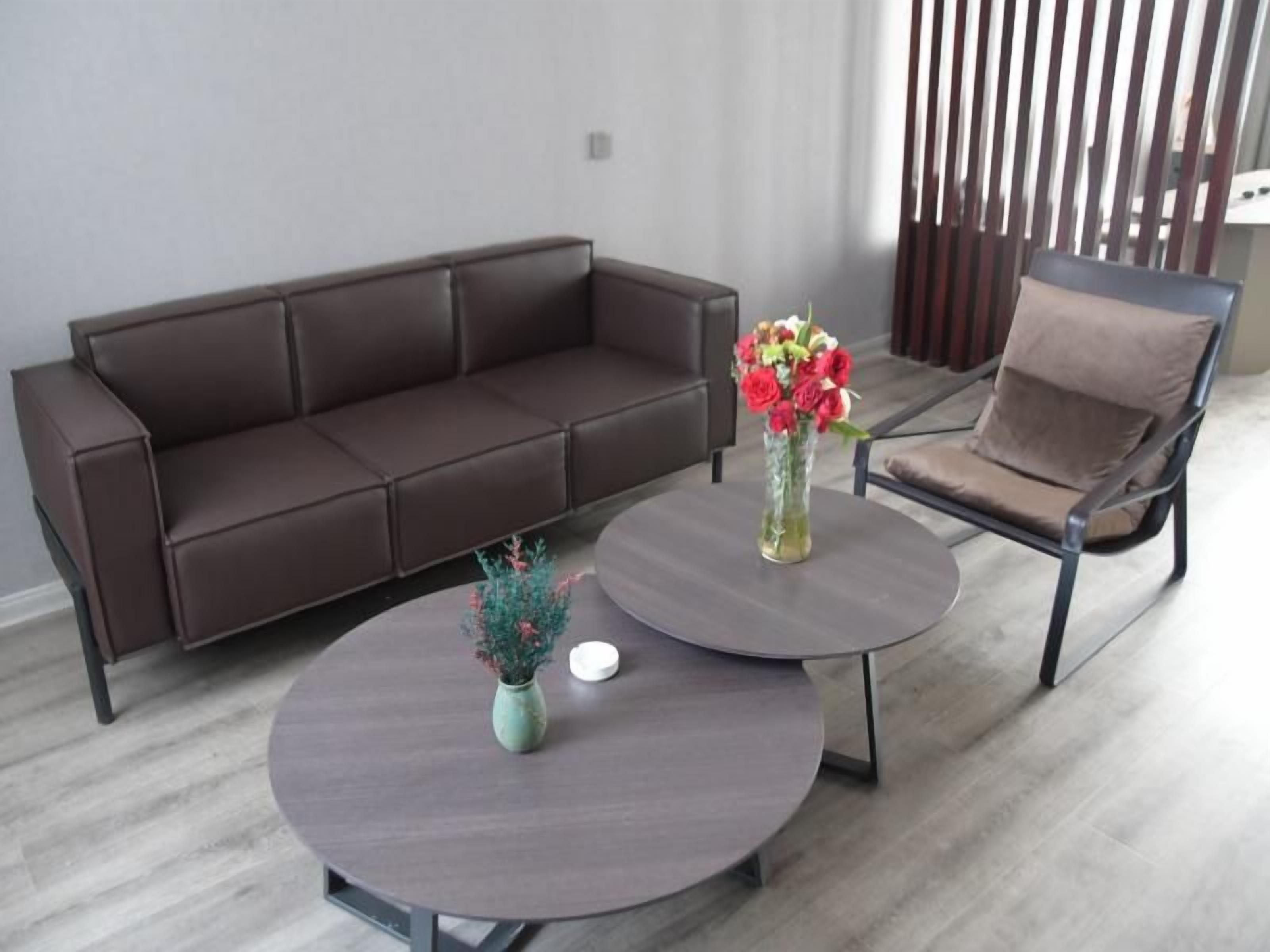 A modern living room with a brown leather sofa, a round coffee table with a vase of flowers, and a brown armchair.