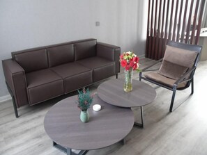 Ein modernes Wohnzimmer mit einem braunen Ledersofa, einem runden Couchtisch mit einer Blumenvase und einem braunen Sessel.