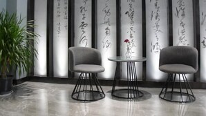 Un intérieur moderne avec deux fauteuils gris, une petite table ronde ornée d’un vase et une plante en pot. Des panneaux verticaux ornés de calligraphie japonaise se trouvent à l’arrière-plan.